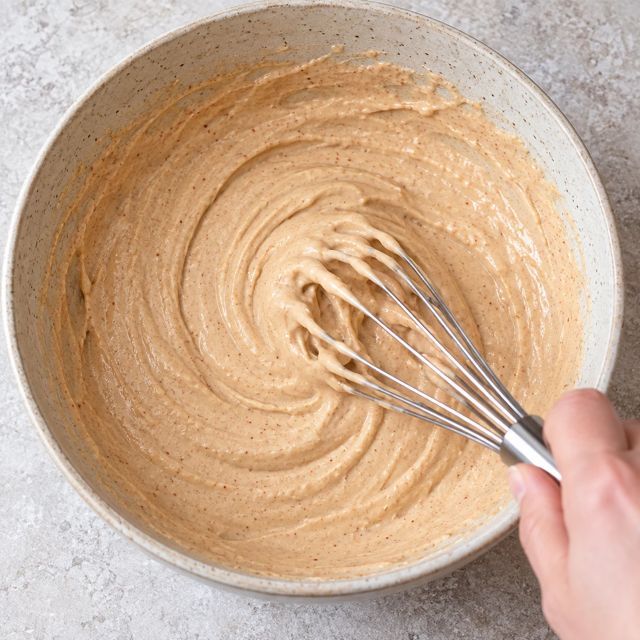 Un fouet mélange une pâte épaisse beige légèrement teintée par le paprika dans un bol neutre.