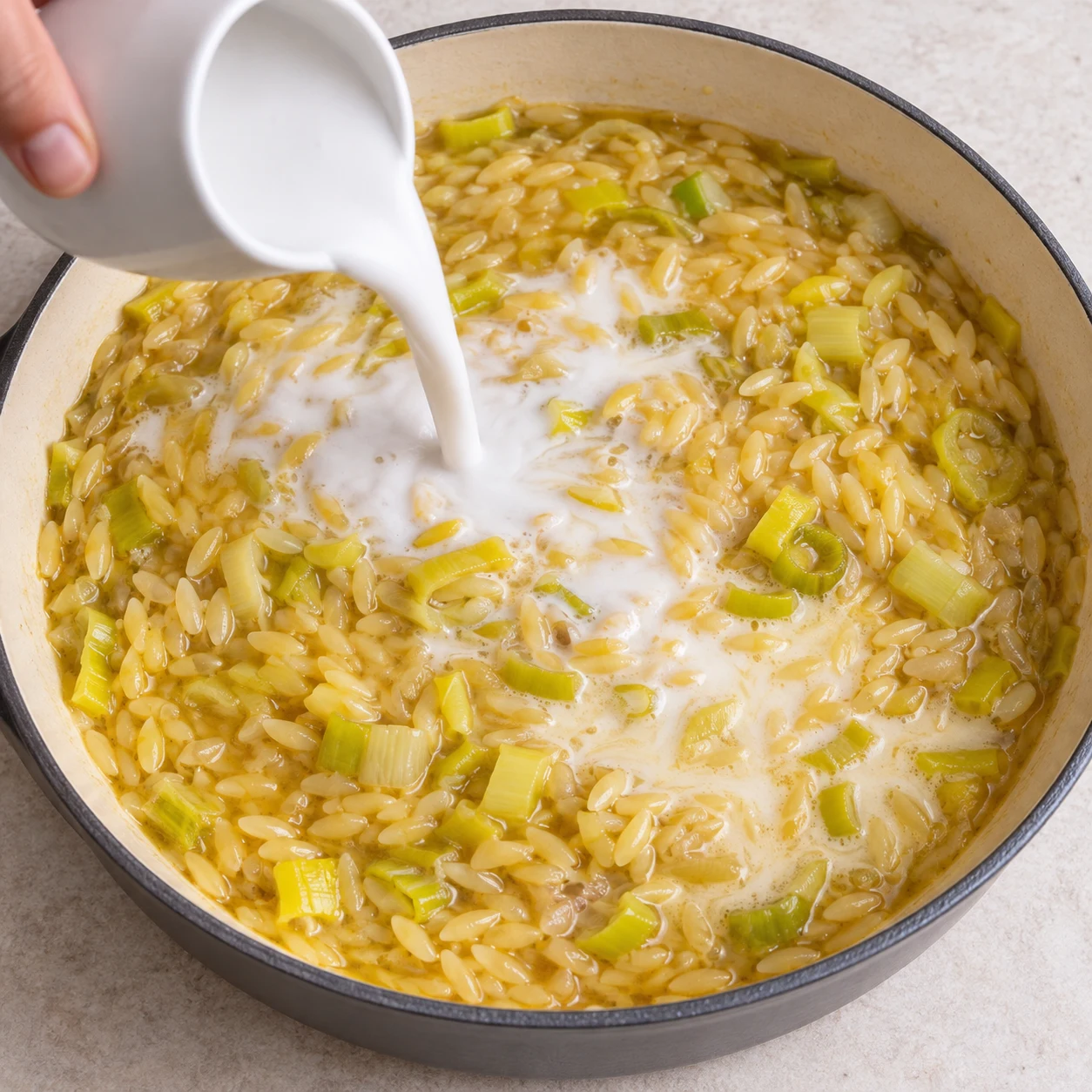 Incorporer le lait de coco. Le lait de coco se répartit dans l’orzo.. Reproduire une seule action, ingrédients exacts et phase exacte. Adapter les crevettes visibles en pois chiches cuits entiers uniquement après son ajout. Aucun ingrédient futur.