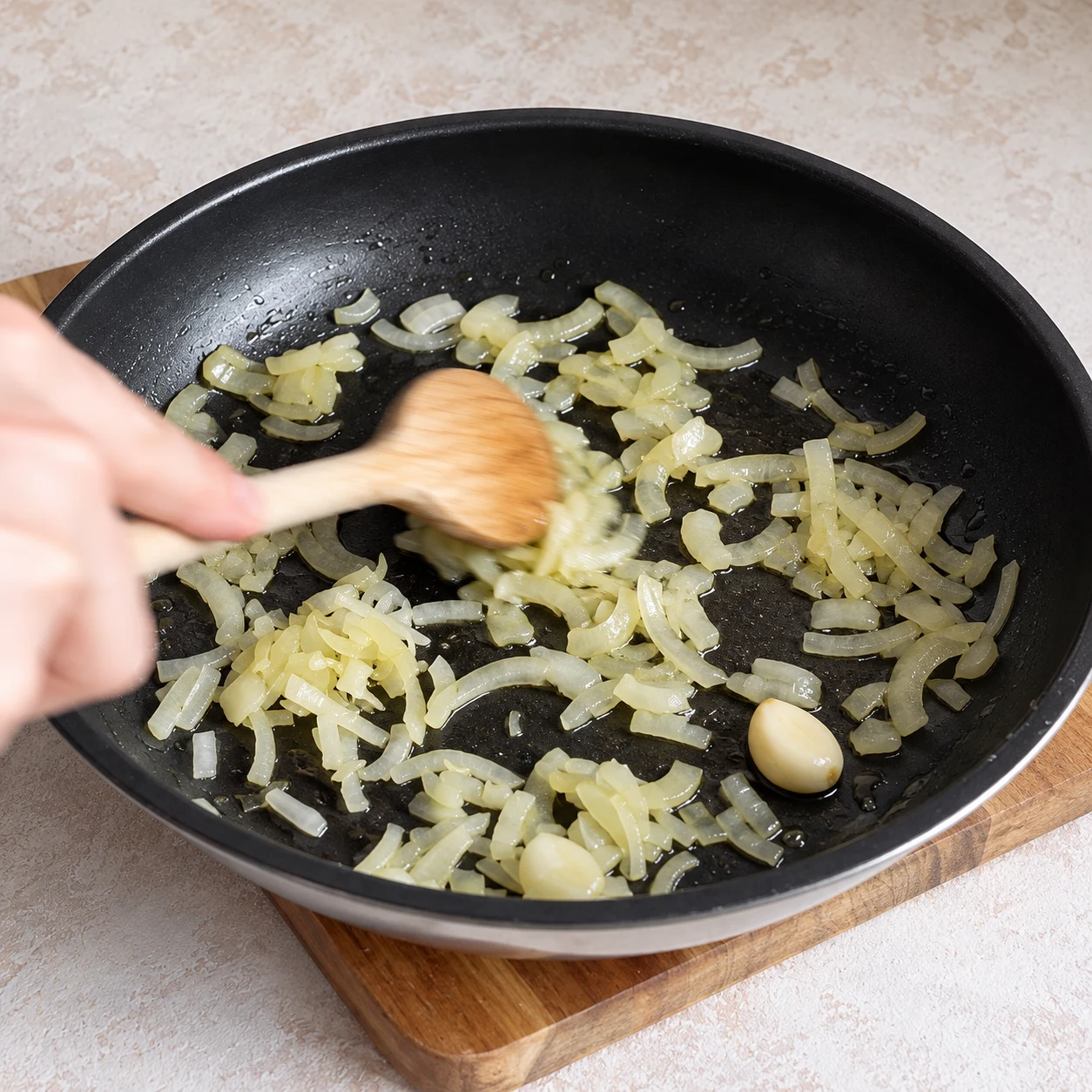 Faites revenir l’oignon avec la gousse d’ail et le filet d’huile d’olive dans une poêle pendant 3 minutes. Une seule scène et une seule phase ; ne montrer que les ingrédients autorisés à cette étape.