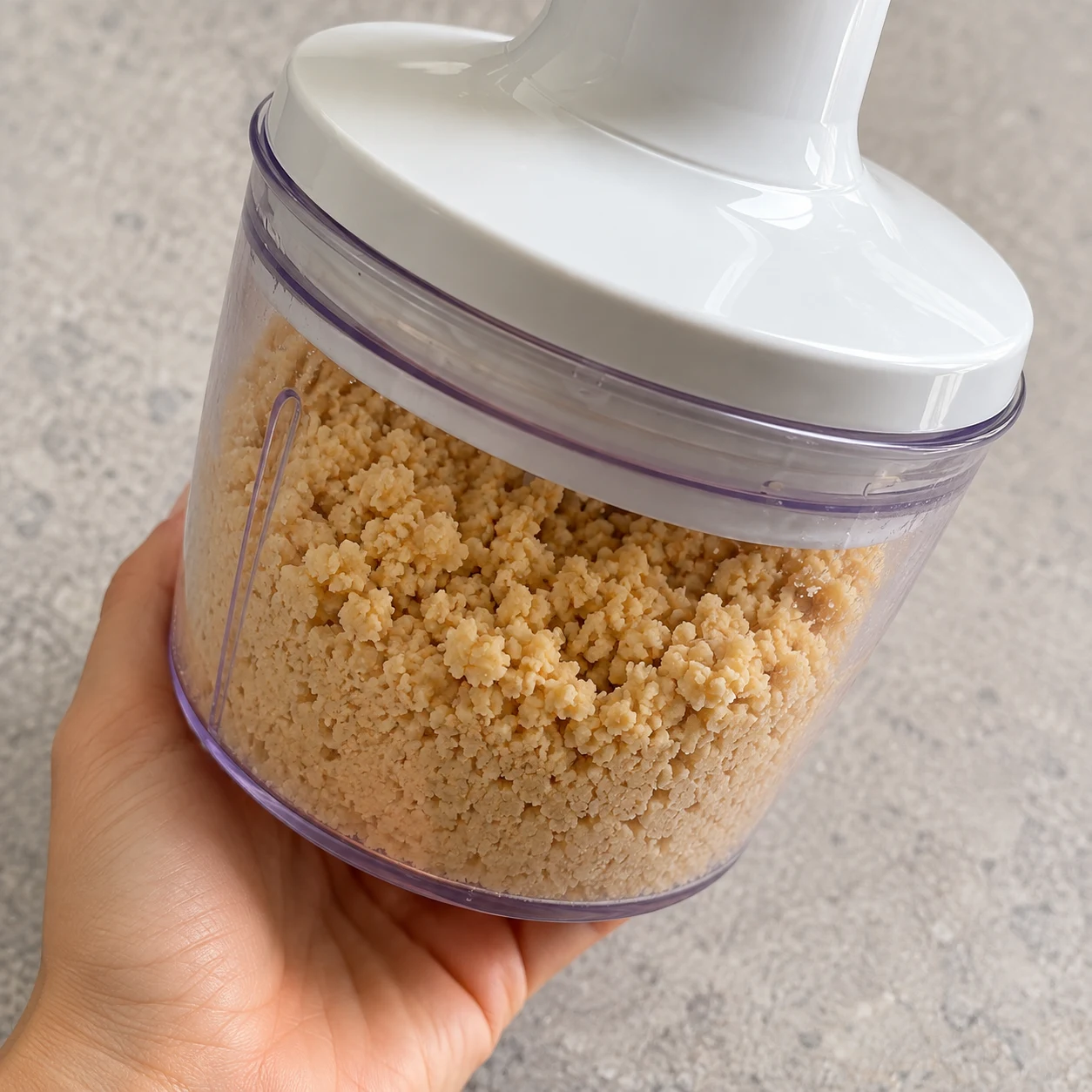 Petit hachoir fermé contenant une mouture beige de pois chiches trempés, encore granuleuse.
