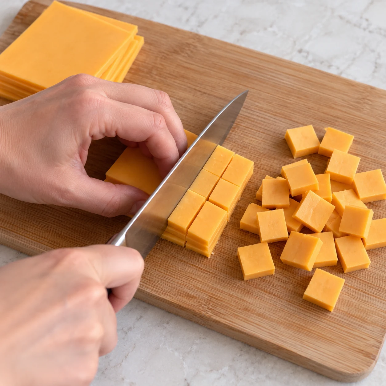 Couper le fromage végétal : Les tranches sont découpées en carrés réguliers faciles à répartir. Ingrédients finaux uniquement, une seule action, photographie carrée réaliste.