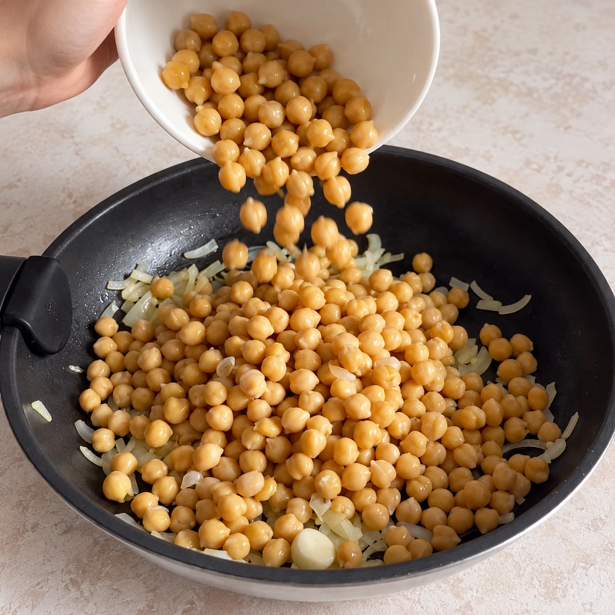 Ajoutez les 250 g de pois chiches en conserve à la poêle. Une seule scène et une seule phase ; ne montrer que les ingrédients autorisés à cette étape.