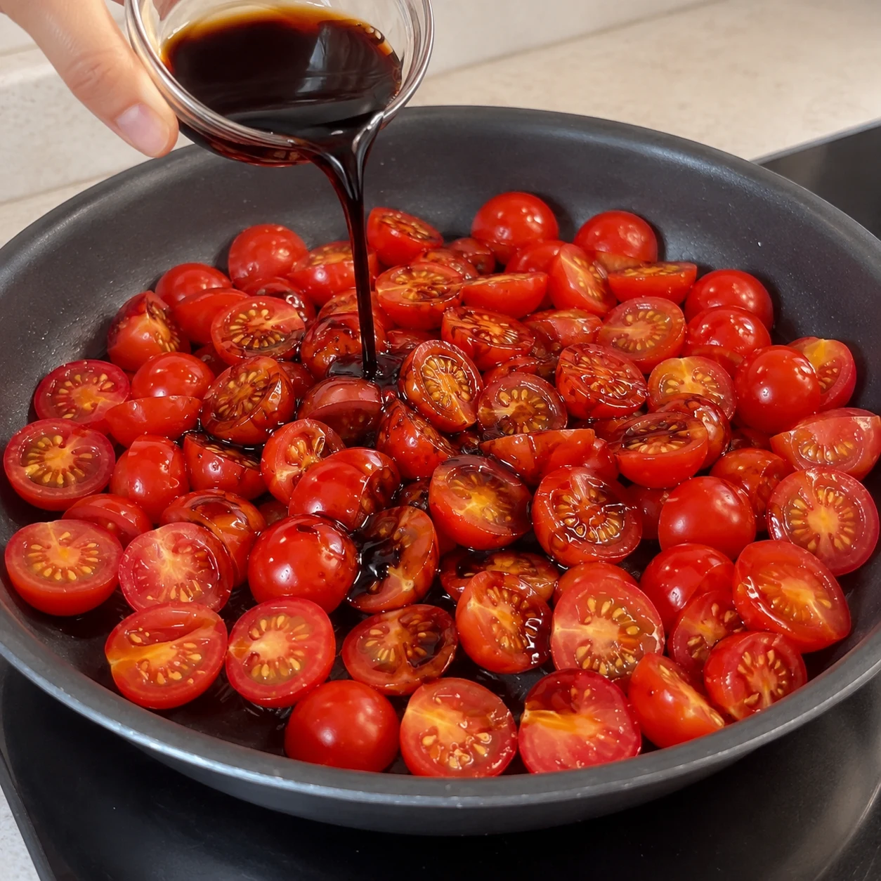 Versez les trois cuillères à soupe de vinaigre balsamique sur les tomates. Montrer une seule phase et aucune personne identifiable.