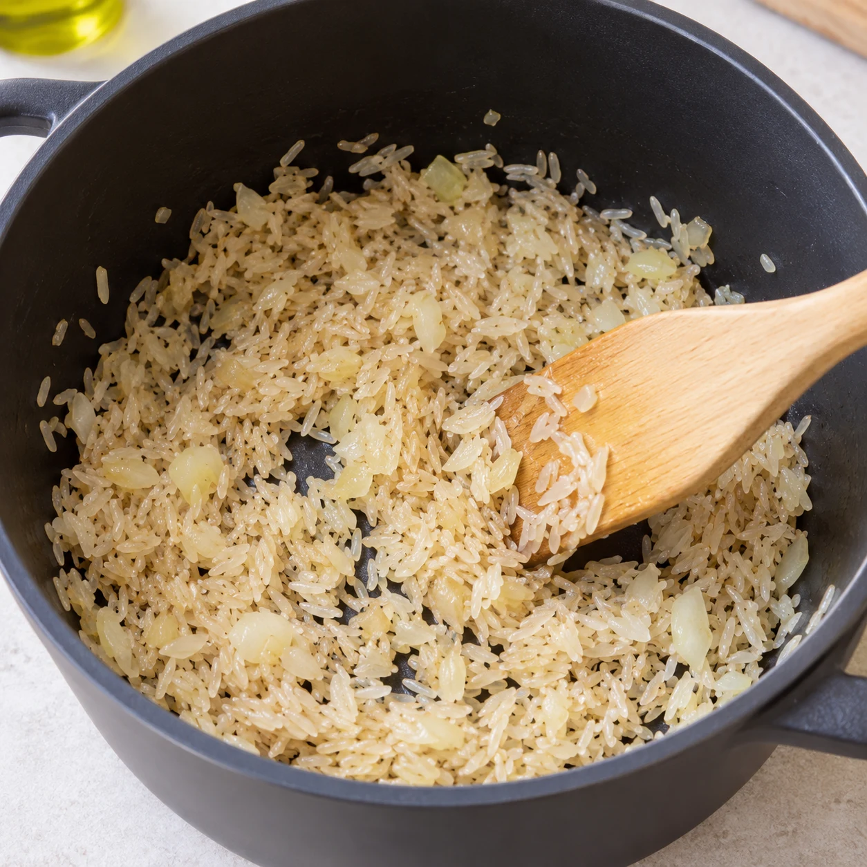 Riz long sec remué avec oignon dans casserole noire ; aucun liquide encore.