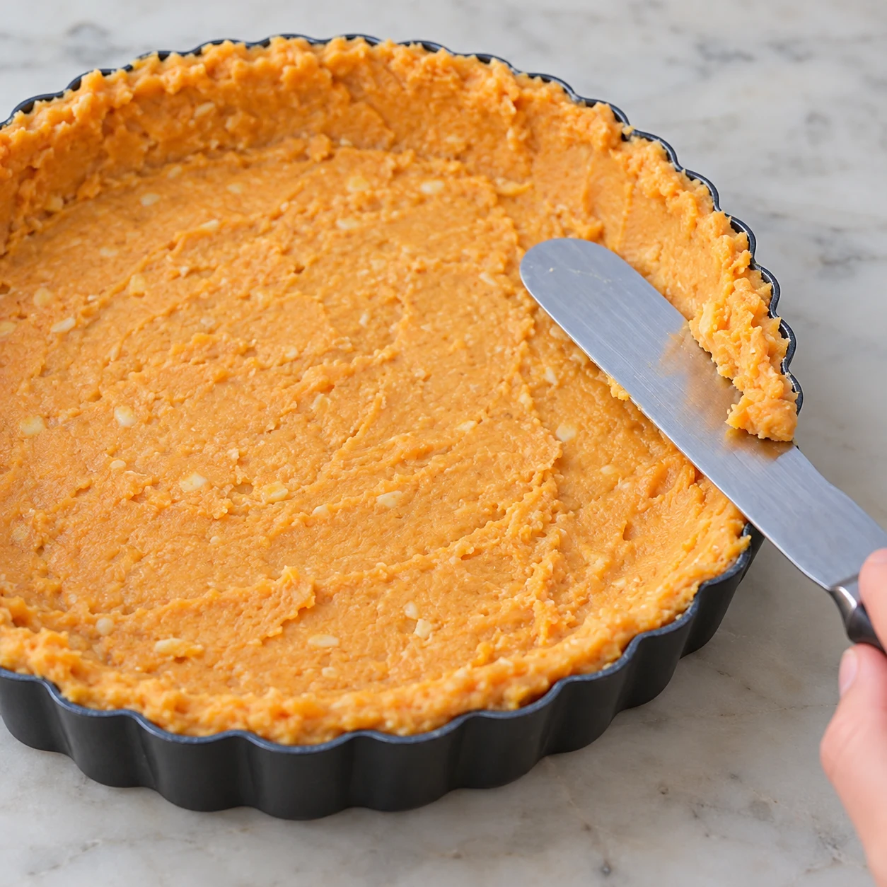 Spatule étalant pâte orange sur fond et bords d’un moule.