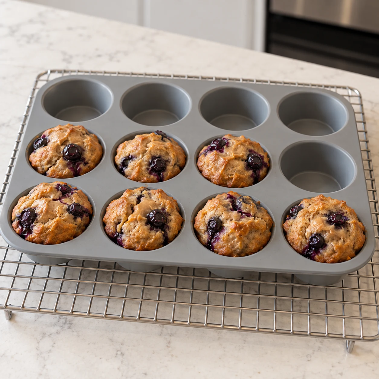 Moule en silicone posé sur une grille, sept muffins cuits dorés avec myrtilles entières, refroidissement après cuisson, sans main ni vapeur excessive.