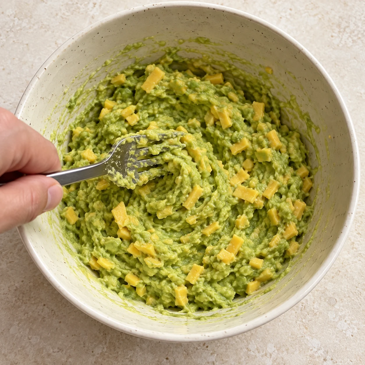 Fourchette mélangeant une purée d’avocat verte et des petits morceaux végétaux jaunes, liaison incorporée ; aucun œuf.