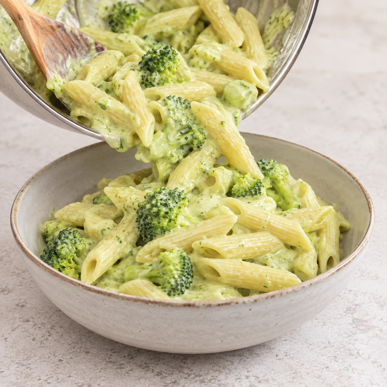 Penne en sauce vert pâle et fleurettes dressées dans un bol en céramique neutre, sans topping.