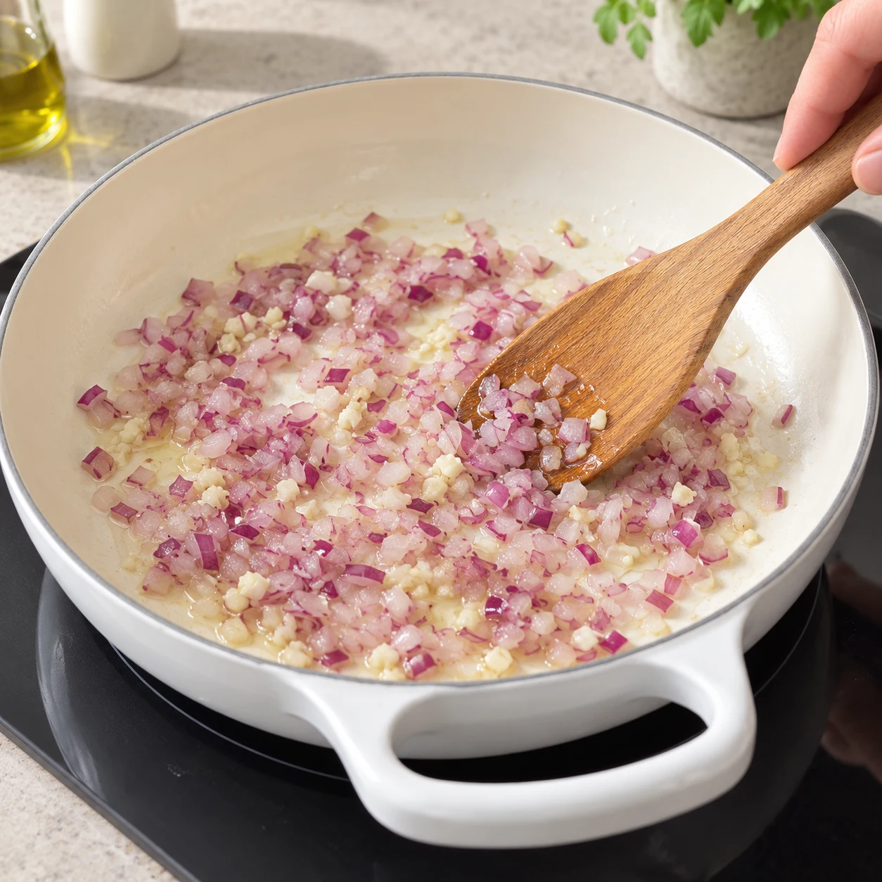 Spatule remuant l’oignon rouge haché et l’ail dans une poêle légèrement huilée.