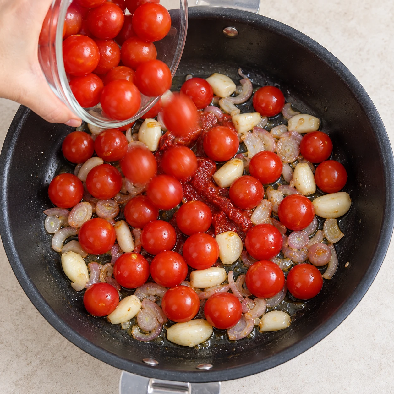 Verse les 400 g de tomates cerises dans la poêle. Les tomates cerises entières sont réparties dans la poêle.