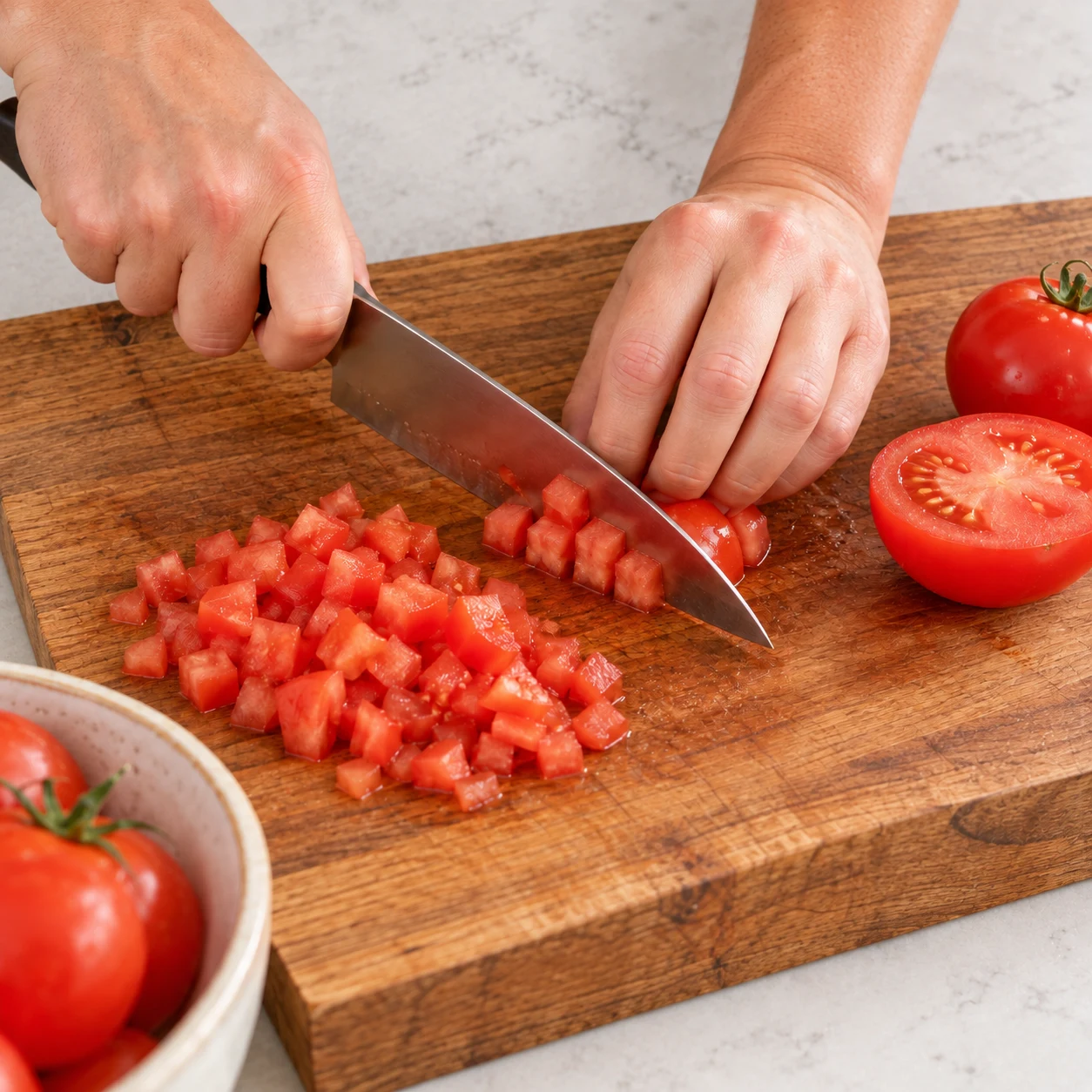 Mains anonymes coupant une tomate fraîche en petits dés, prise en griffe sûre.