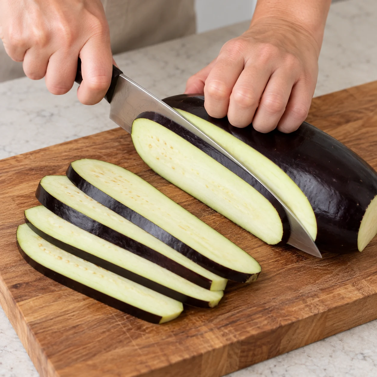 Coupe l’aubergine en lamelles dans la longueur, sur une planche stable. Replie les doigts de la main qui tient le légume. Résultat visible : Les lamelles sont d’épaisseur proche, avec leur peau conservée.