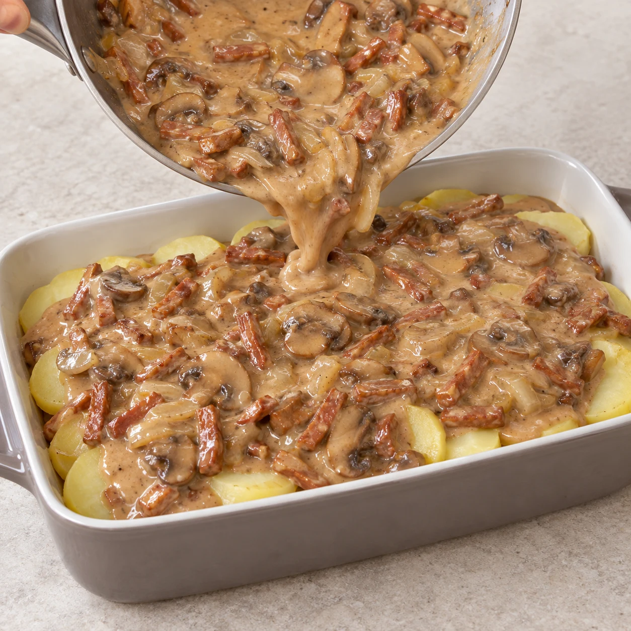 Une seule action : Recouvrir de sauce. La sauce est répartie sur les pommes de terre. Uniquement les ingrédients de cette phase : Pommes de terre, Oignon, Champignons de Paris, Lardons végétaux fumés, Huile végétale, Sauce soja salée, cassonade, Sirop d’érable, Fécule de maïs, Eau froide, Tahini blanc, Levure maltée. Allumettes végétales fumées rosées à base de soja ; jamais de tofu ni de miso. Sauce onctueuse brun clair au sésame, plus pâle que dans la source.