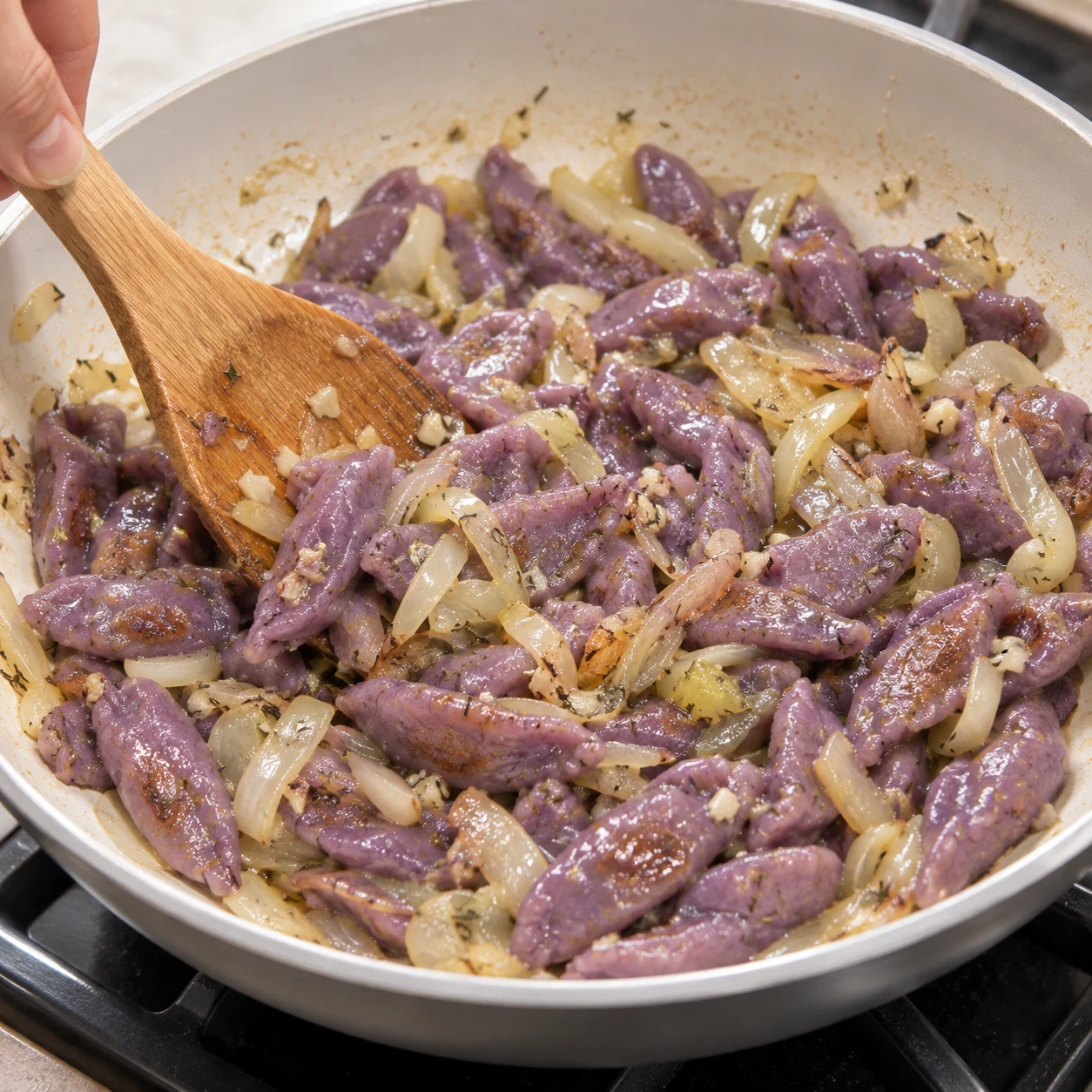 Pâtes mauves courtes aux bords légèrement dorés remuées dans la sauce à l’oignon et à le thym séché.