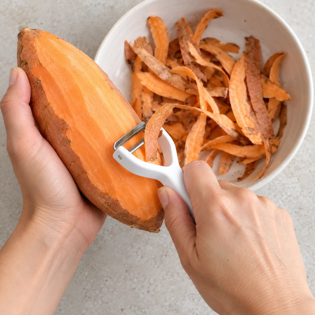 Économe en train de retirer la peau orange-brune d’une patate douce ; chair orange visible.