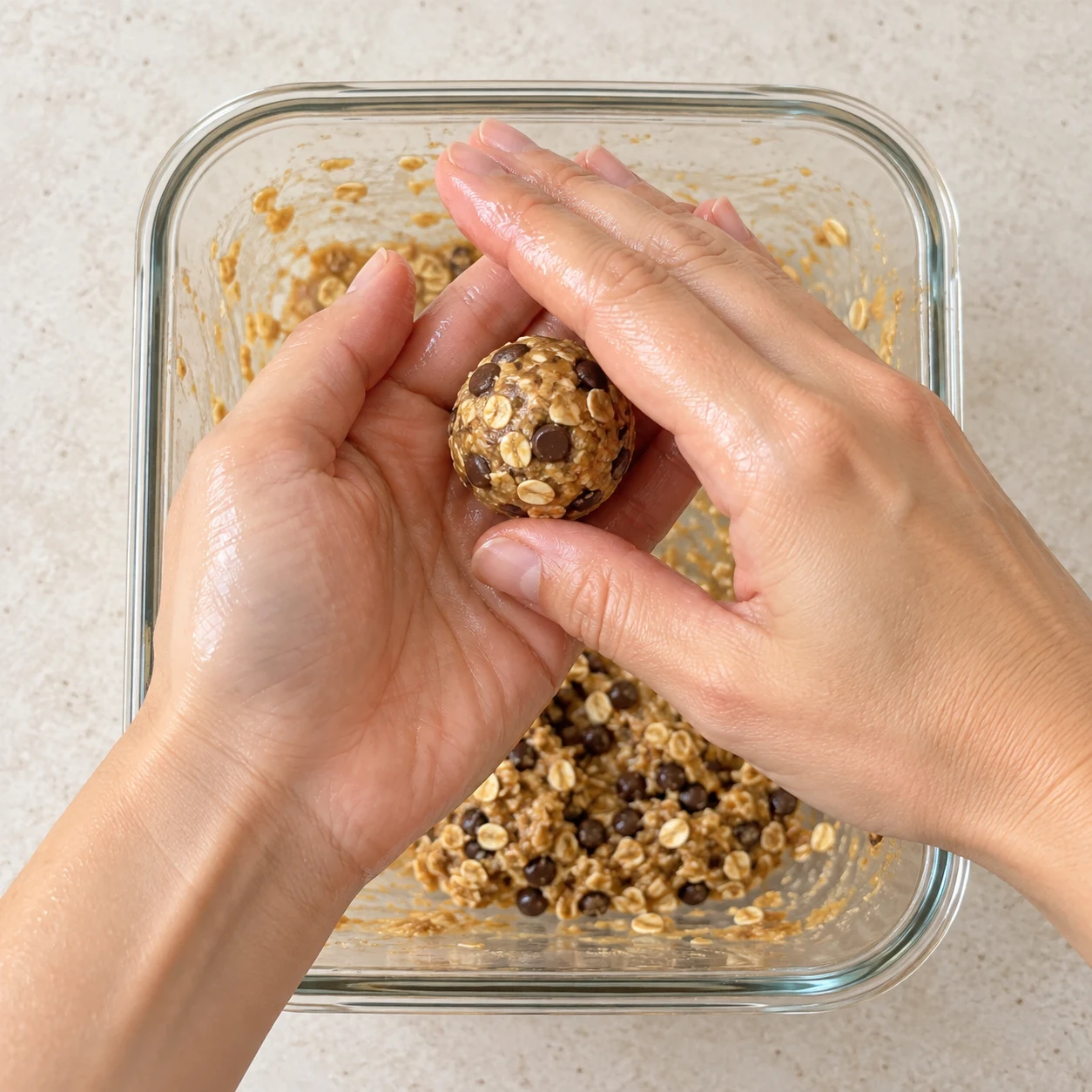 Deux mains adultes anonymes roulent une seule boulette au-dessus du récipient contenant la pâte.