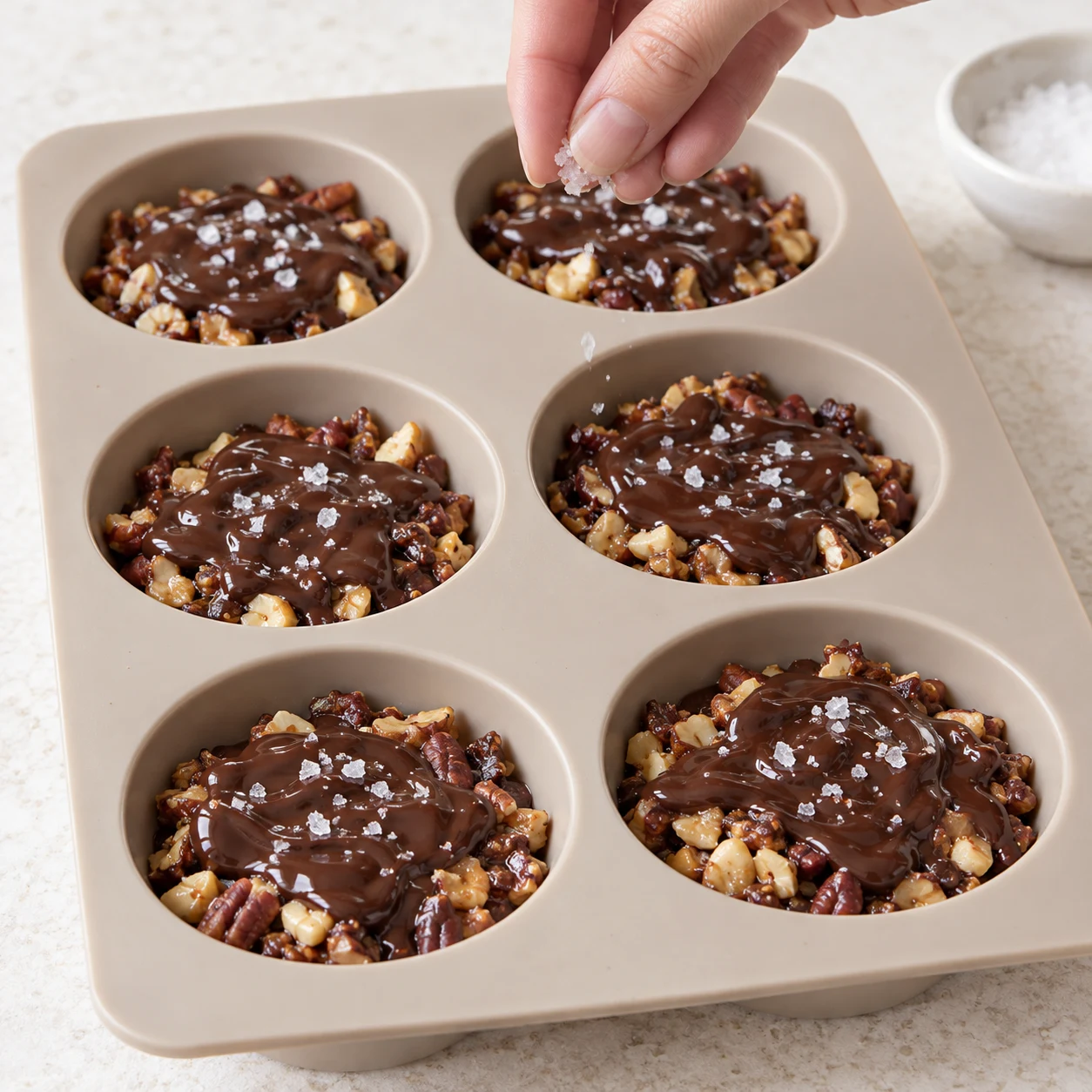 Doigts anonymes dispersant quelques grains de fleur de sel sur les six palets chocolatés.