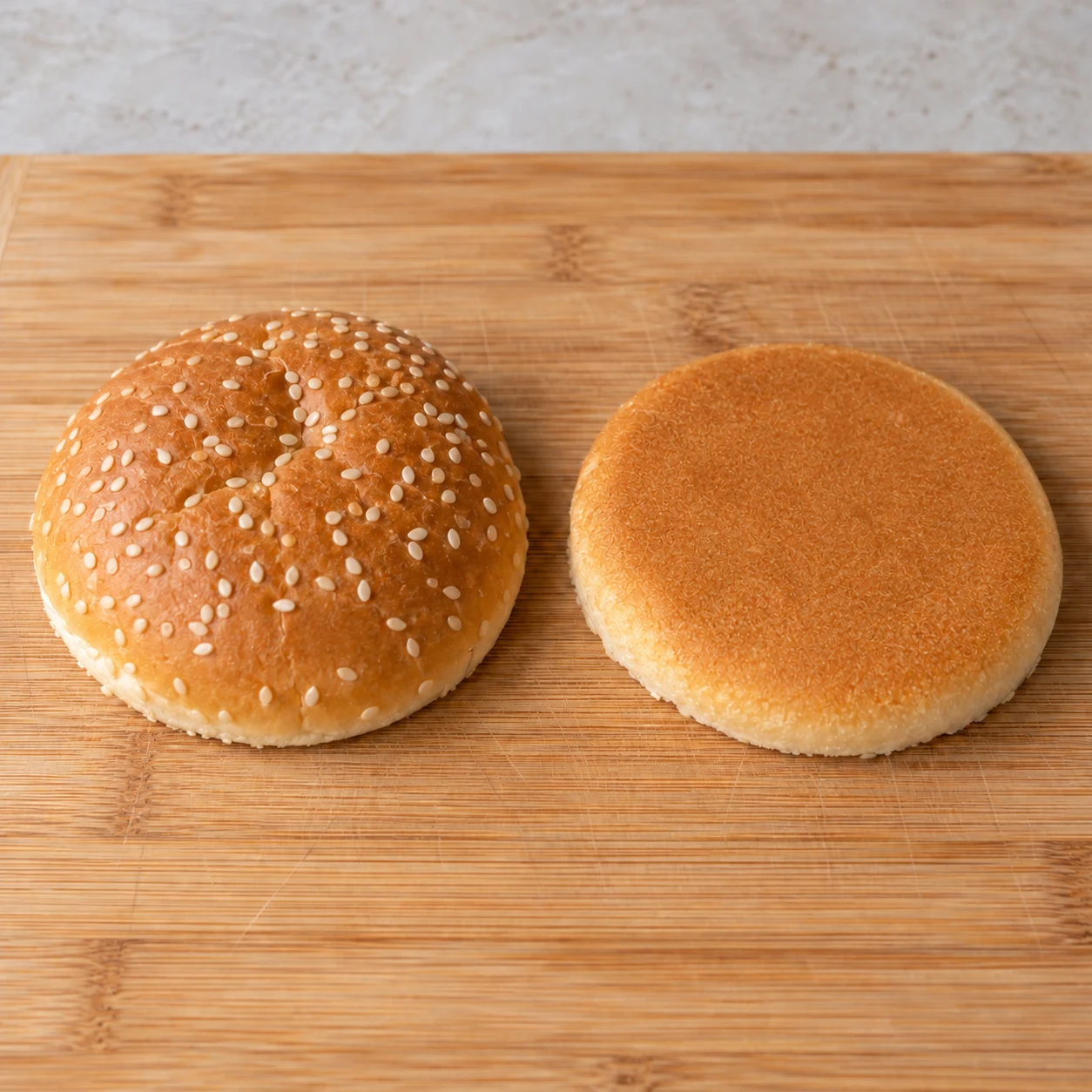 Un seul pain burger séparé en deux moitiés, croûtes vers le haut et mie contre la planche.