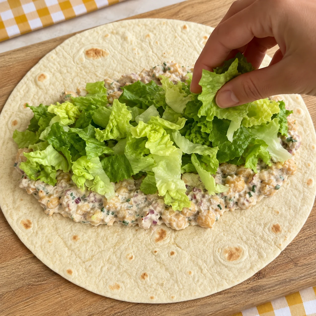 Tortilla ouverte portant la garniture crémeuse aux pois chiches et une poignée de salade verte, sans carotte ni avocat.