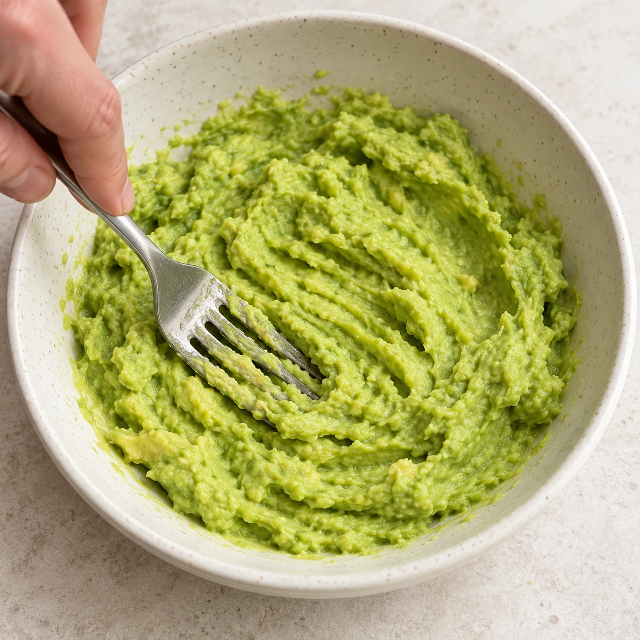 Fourchette écrasant la chair d’avocat seule, purée verte épaisse.