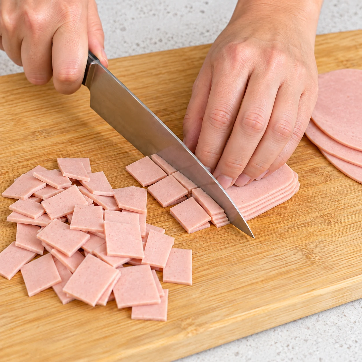 Mains anonymes découpant des tranches végétales roses en petits carrés sur planche, aucun produit animal.