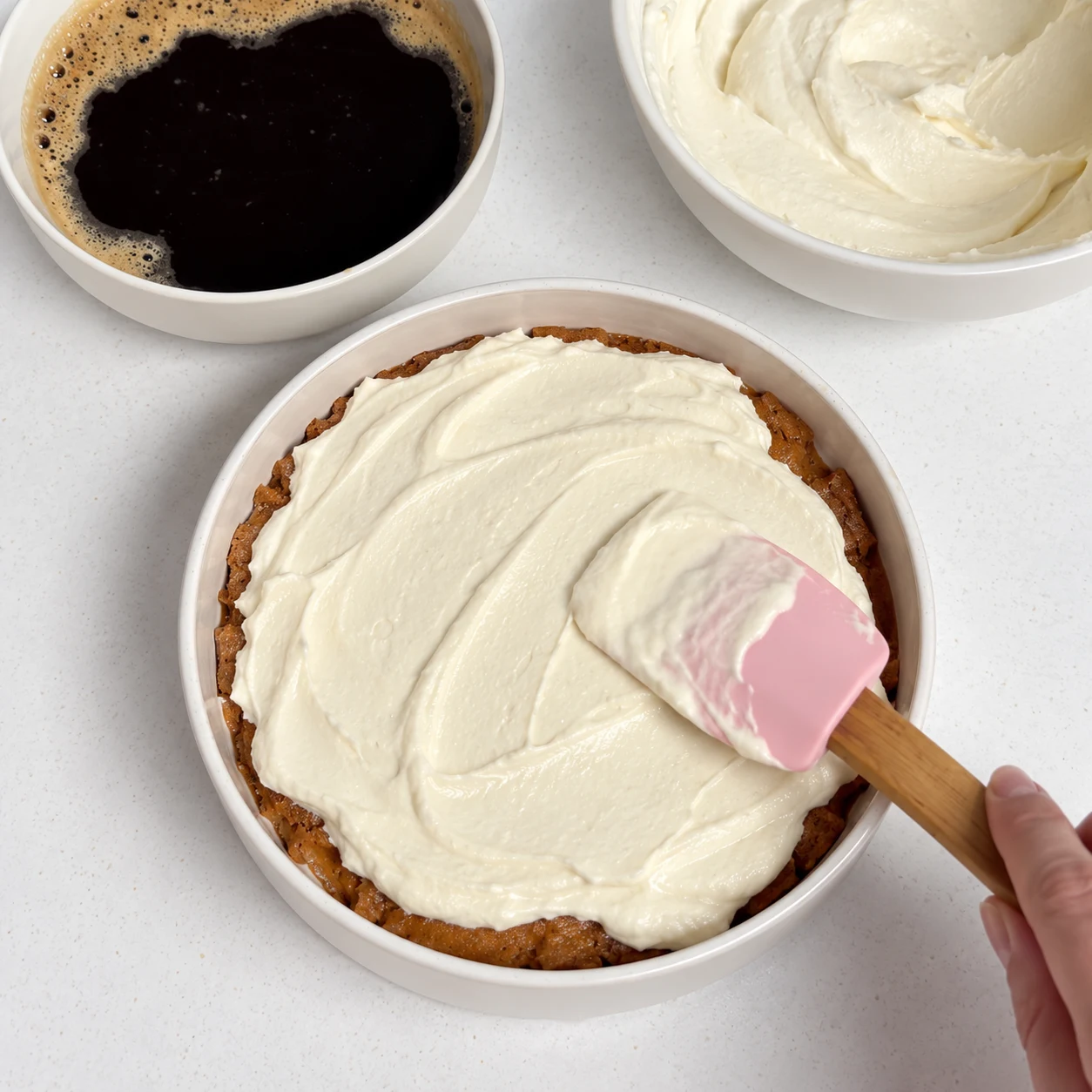Crème ivoire étalée à la maryse sur une couche de spéculoos imbibés dans un plat rond, bol de café à côté.