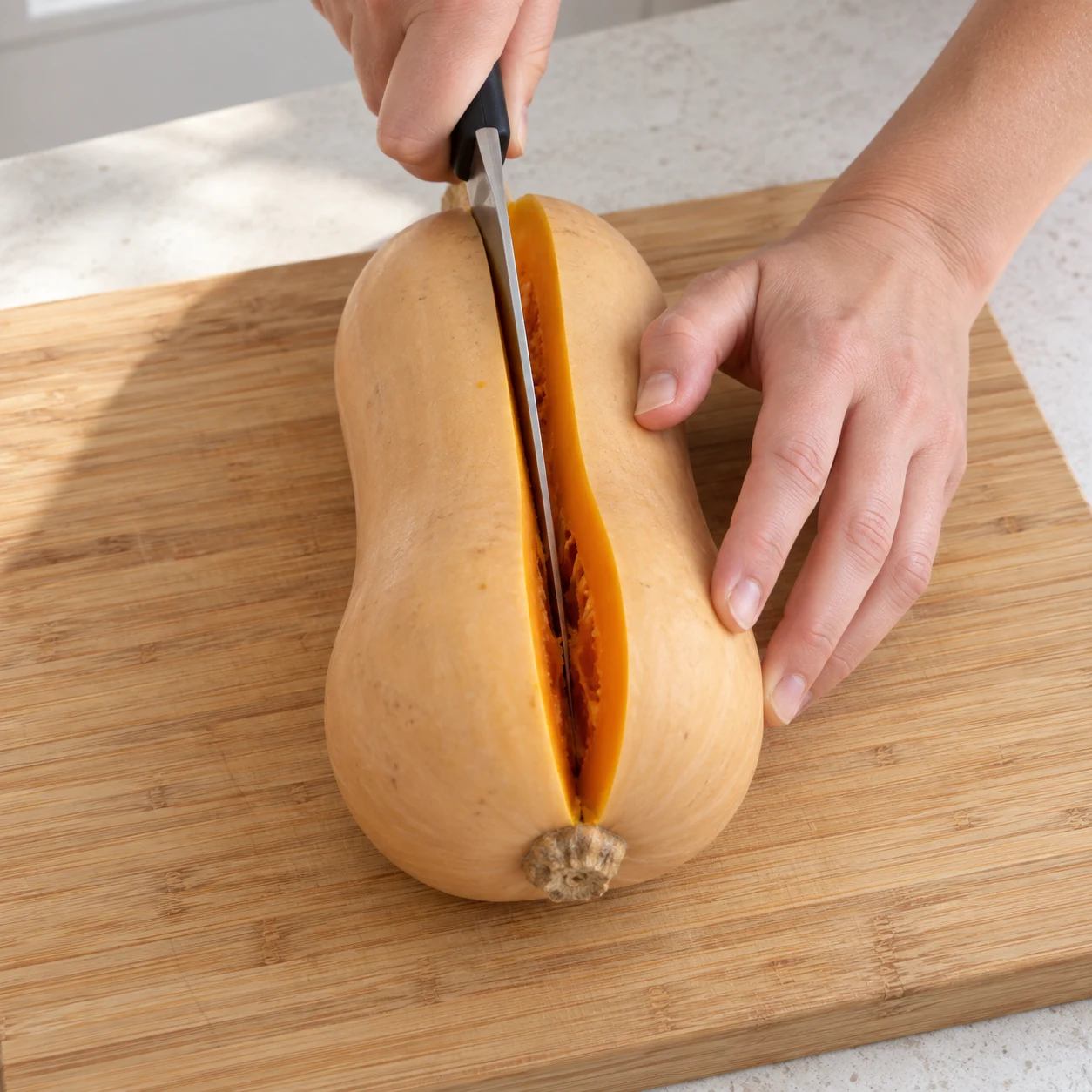 Posez le butternut sur une planche stable et coupez-le en deux dans la longueur, les doigts éloignés de la lame. Montrer une seule phase et uniquement les ingrédients cités.
