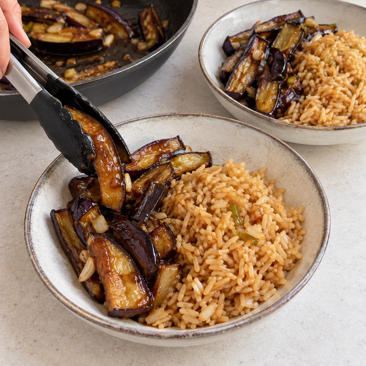 Dispose les aubergines caramélisées à côté du riz dans les deux assiettes. Résultat visible : Les lamelles sont réparties entre les deux assiettes, avec leur sauce.