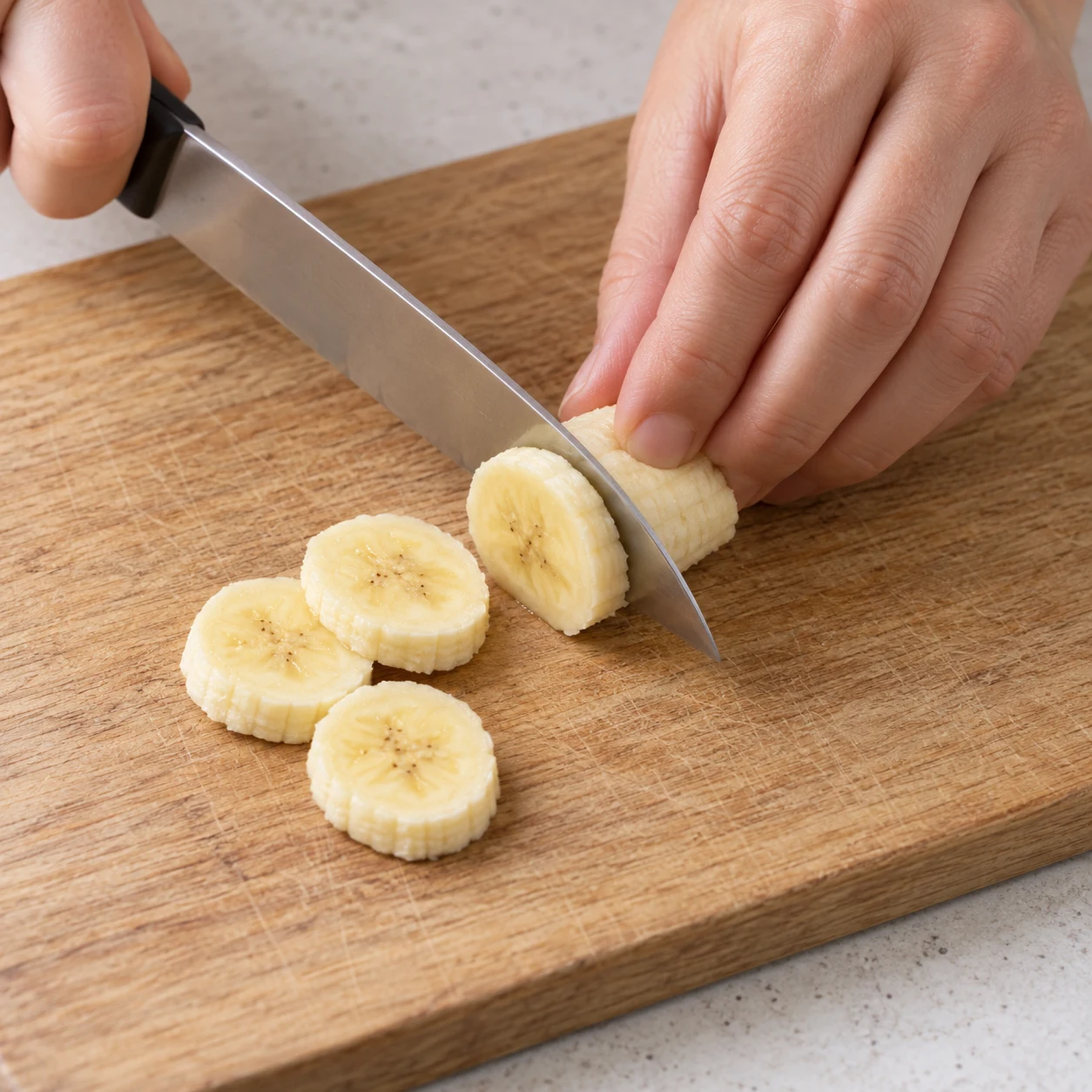 Découpe sûre de rondelles de banane sur une planche ; pas de bocal ni de flocons dans ce cadrage.
