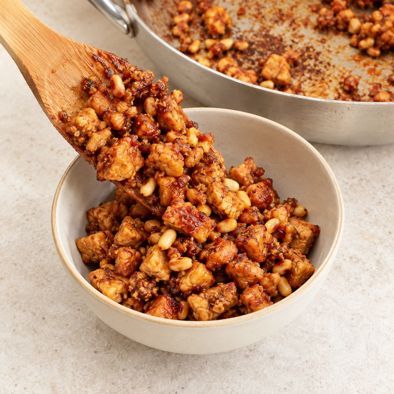 Crumble de tempeh caramélisé avec des pignons transféré à la spatule dans un bol en céramique.