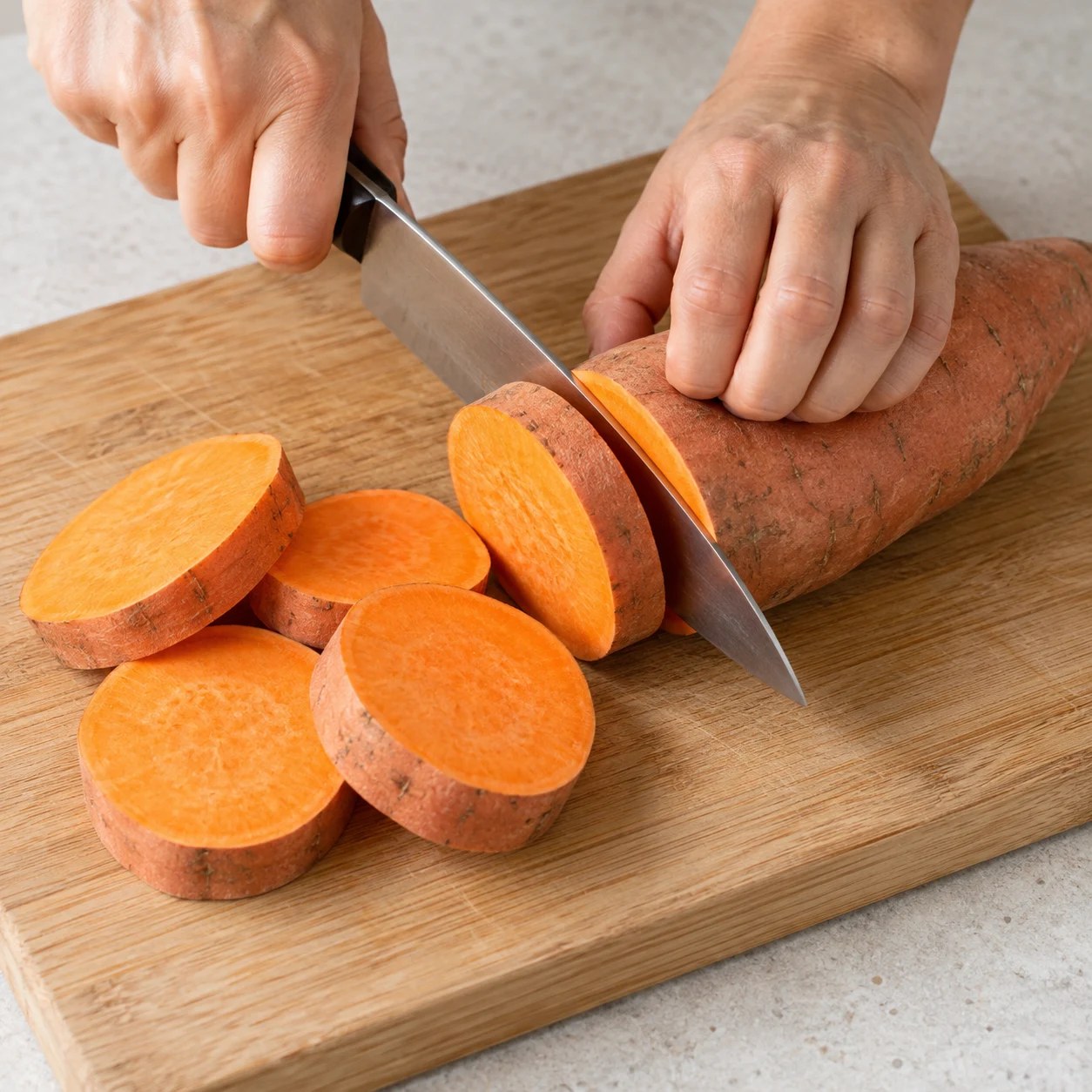 Une photographie carrée de cette seule action : Sur une planche stable, coupe les 800 g de patate douce en tranches épaisses, les doigts repliés à distance de la lame. Résultat attendu : Les patates douces sont découpées en tranches épaisses. Seulement les ingrédients de cette étape. Aucun ingrédient futur ni garniture ajoutée, aucun texte ni personne identifiable. Mains adultes anonymes seulement pour le geste.