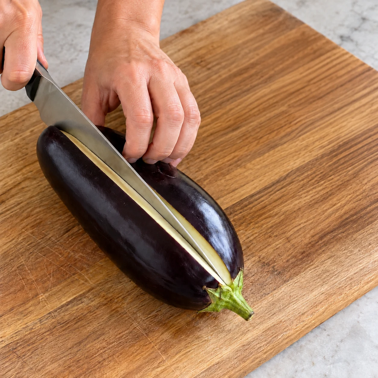 Aubergines crues violettes, coupe longitudinale en cours ; couteau et prise en griffe sûrs.