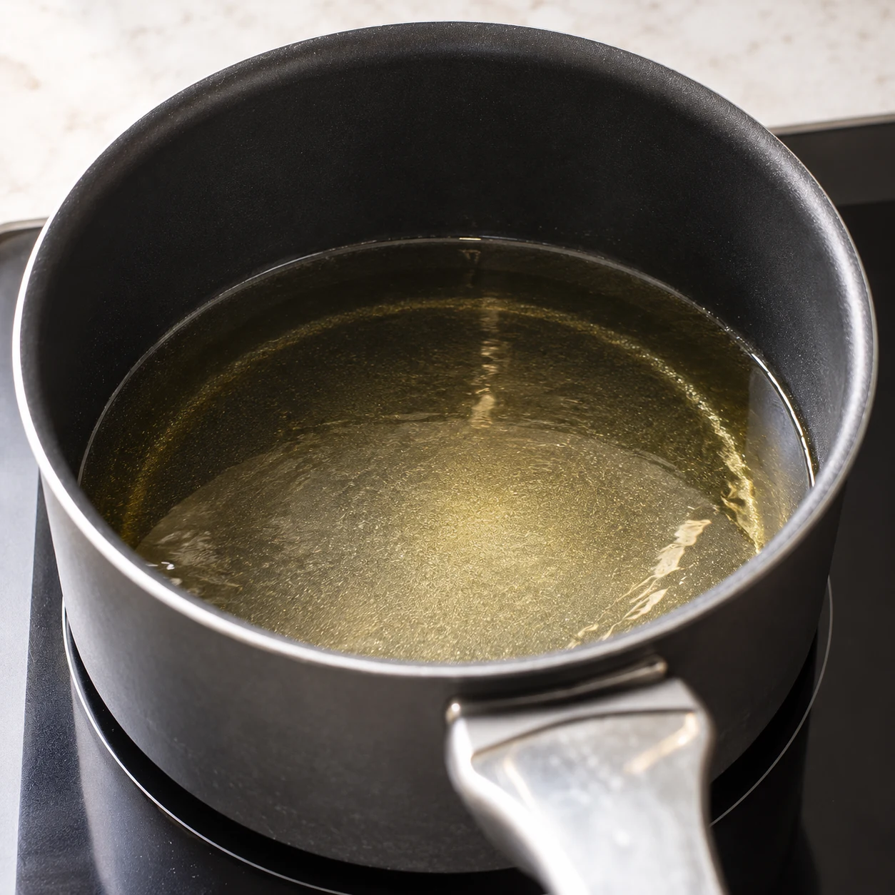 Bain d’huile claire dans une casserole noire à bords hauts sur une plaque ; aucune pâte ni oignon, aucun thermomètre ni chiffres. Référence d’apparence : huile versée à 26 s ; chauffage inhérent à la friture décrite par la recette d’origine.