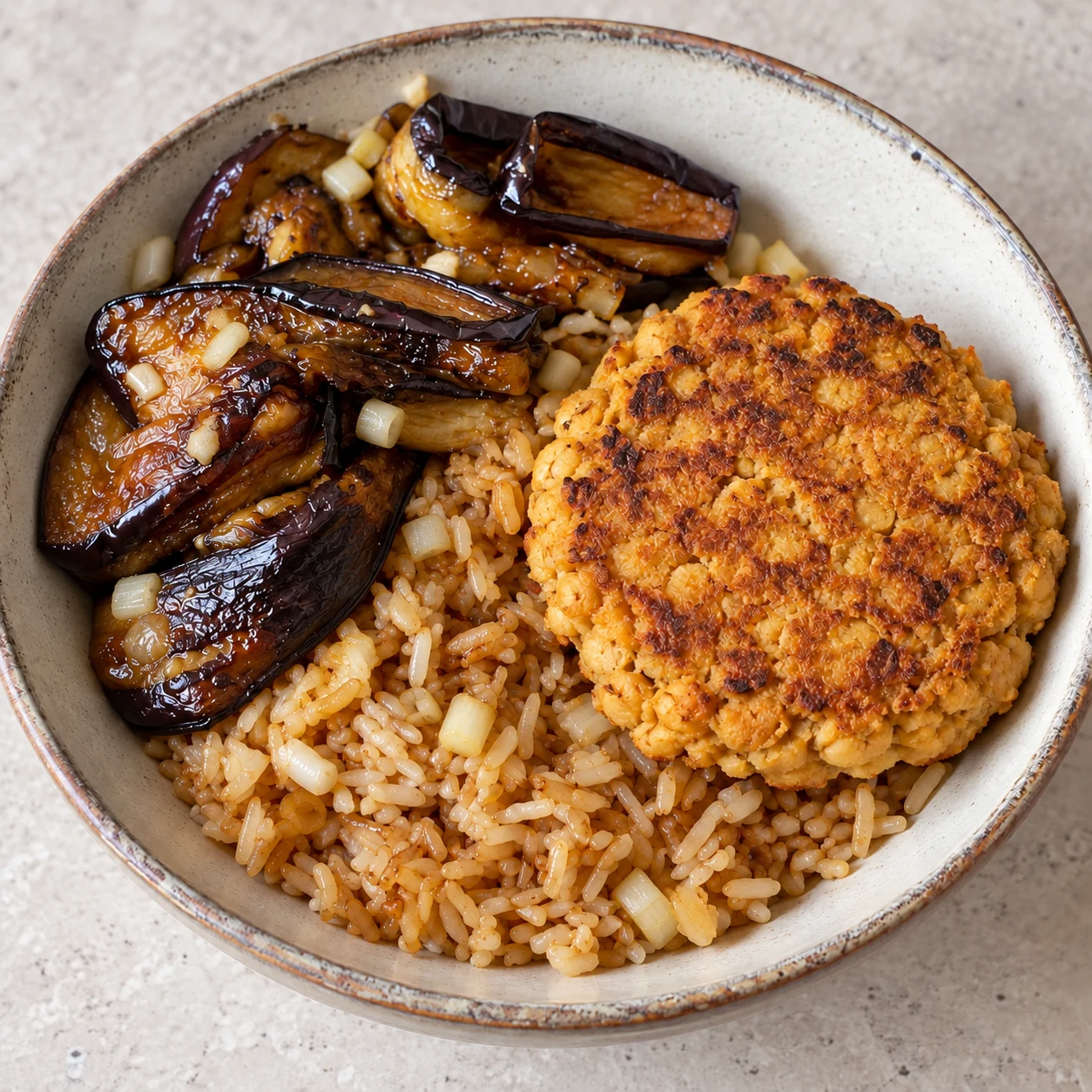 Pose une galette de pois chiche sur chaque assiette, à l’emplacement de l’œuf au plat de la source. Résultat visible : Chaque assiette contient une galette cuite, du riz et des aubergines.