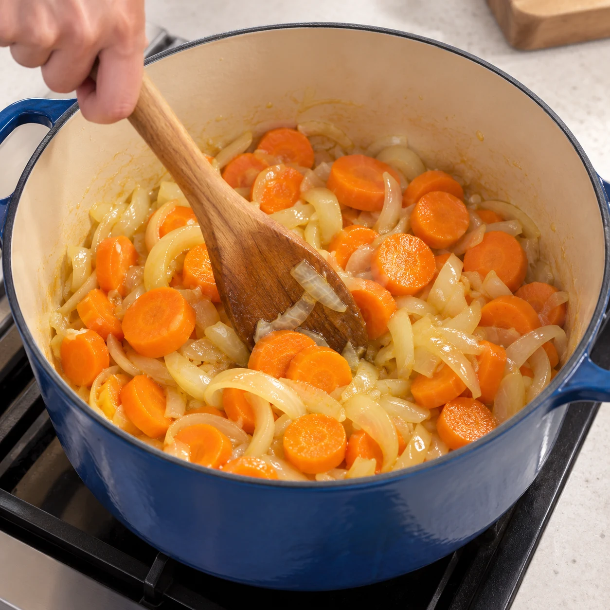Spatule remuant carottes en rondelles et oignons dans la cocotte.