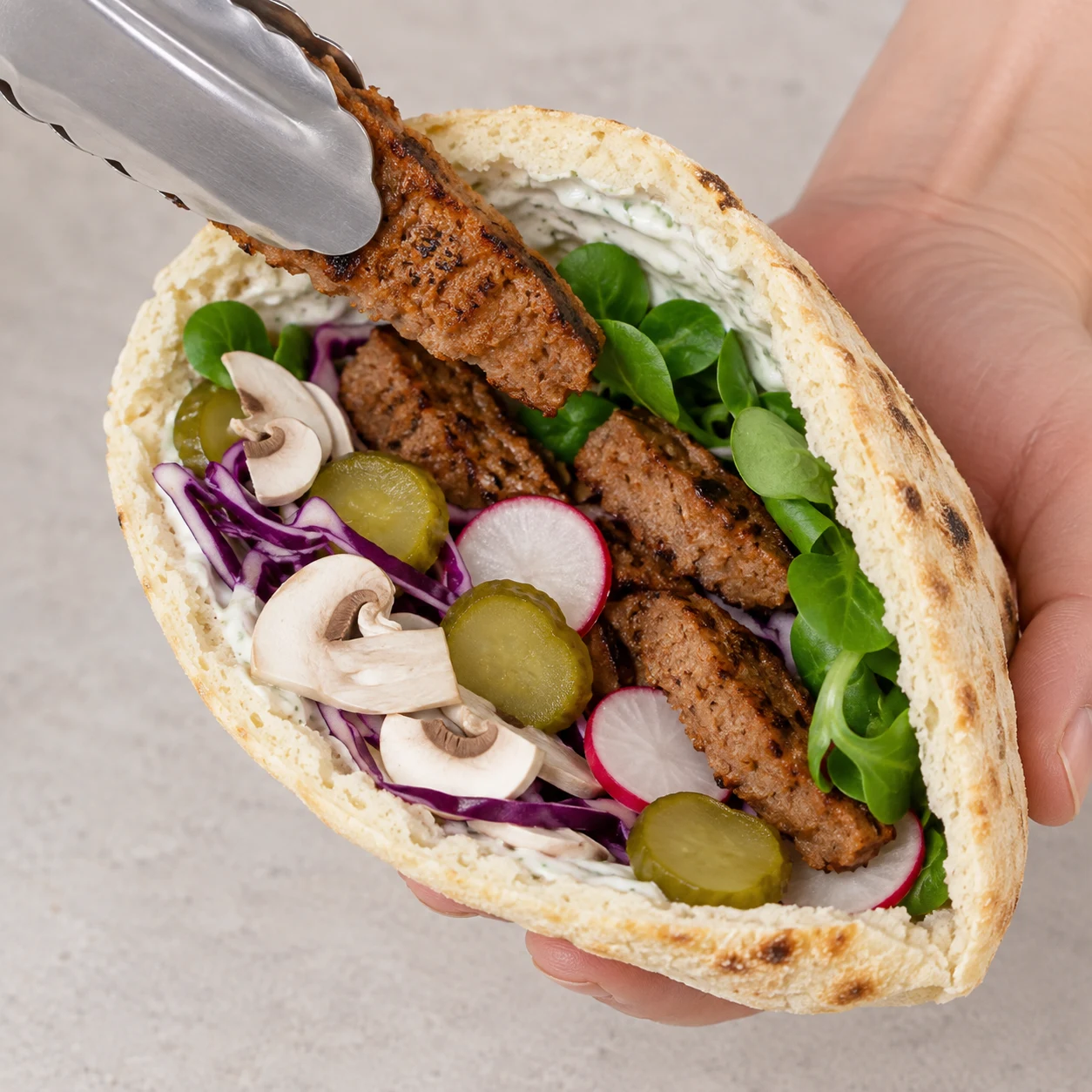 Garnir les six pitas. Chaque pita contient salade, chou, champignons, steaks végétaux, radis et cornichons, maintenus dans la poche.