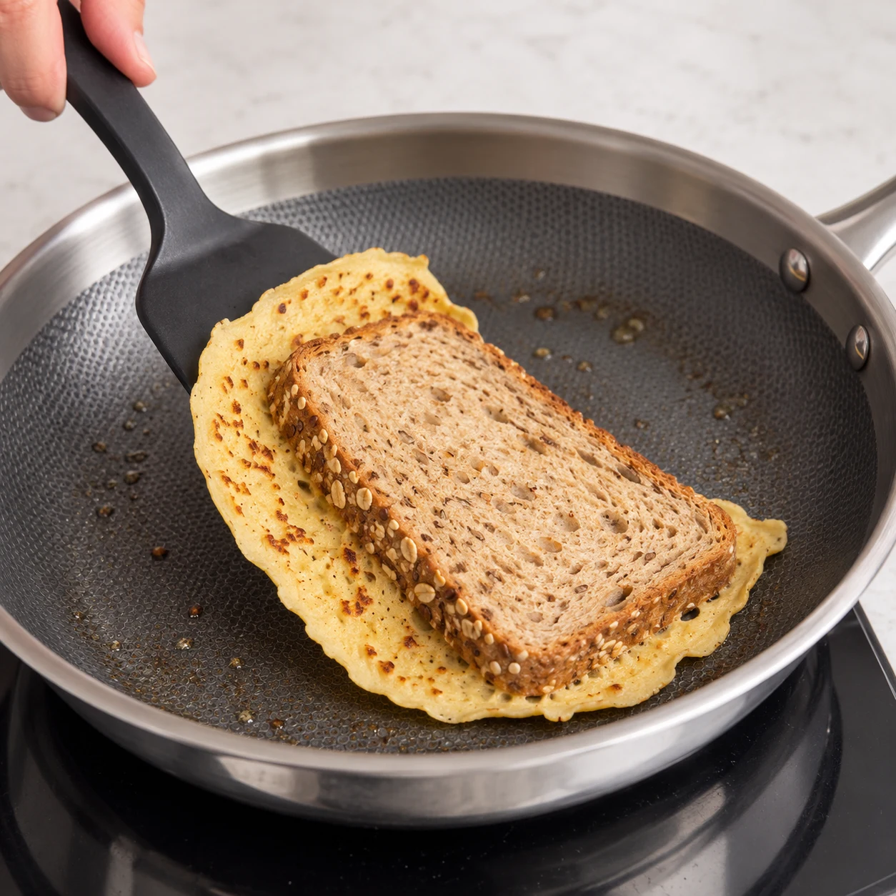 Spatule retournant une tranche de pain de mie aux céréales attachée à une fine galette beige.