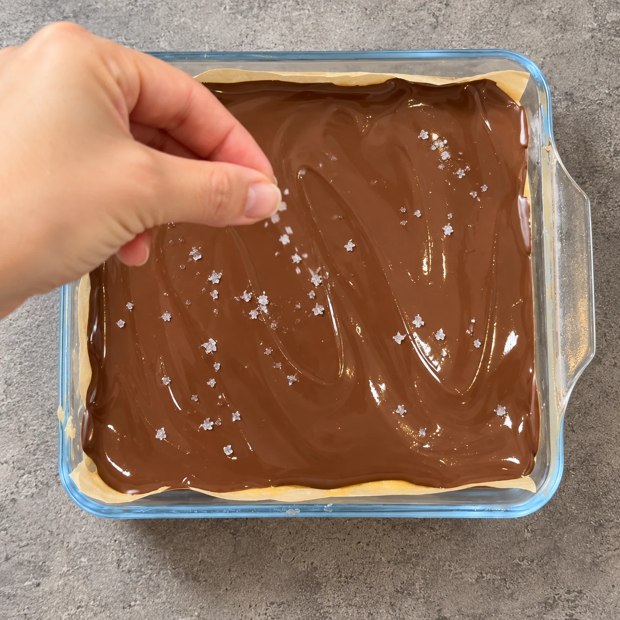 Main anonyme saupoudrant quelques cristaux de fleur de sel sur le chocolat encore brillant.