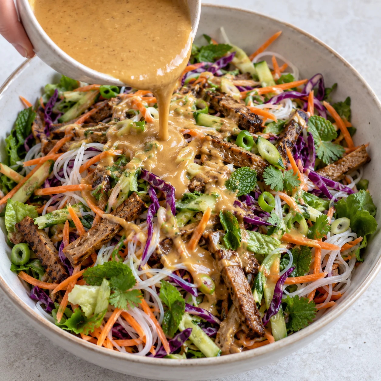Photographie carrée de cette seule action ou son résultat : Ajouter la sauce. La salade servie immédiatement est enrobée de sauce ; pour le lendemain, la sauce reste à part. Seulement les ingrédients visibles de cette étape. La référence source contient du poulet : remplacer uniquement la protéine par les lamelles végétales de steaks pois et fèveroles. Aucun produit animal, texte ni personne identifiable.