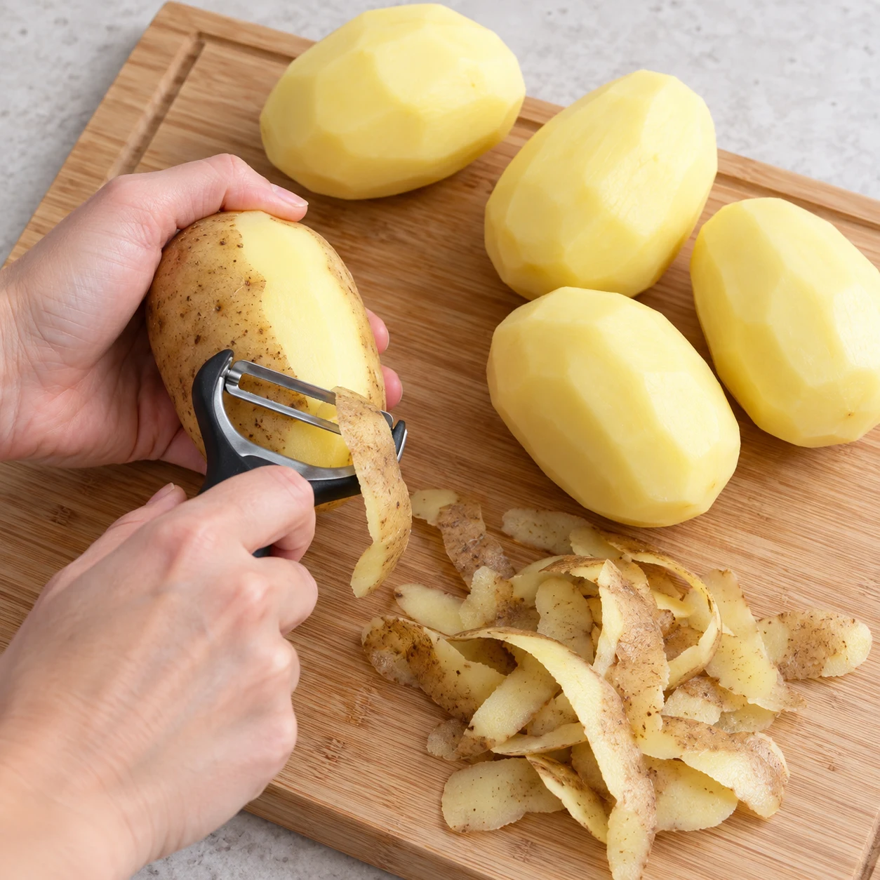 Épluchez les 5 grosses pommes de terre avec un économe. Montrer seulement cet état, sans personne identifiable, visage, texte, logo ni ingrédient futur.