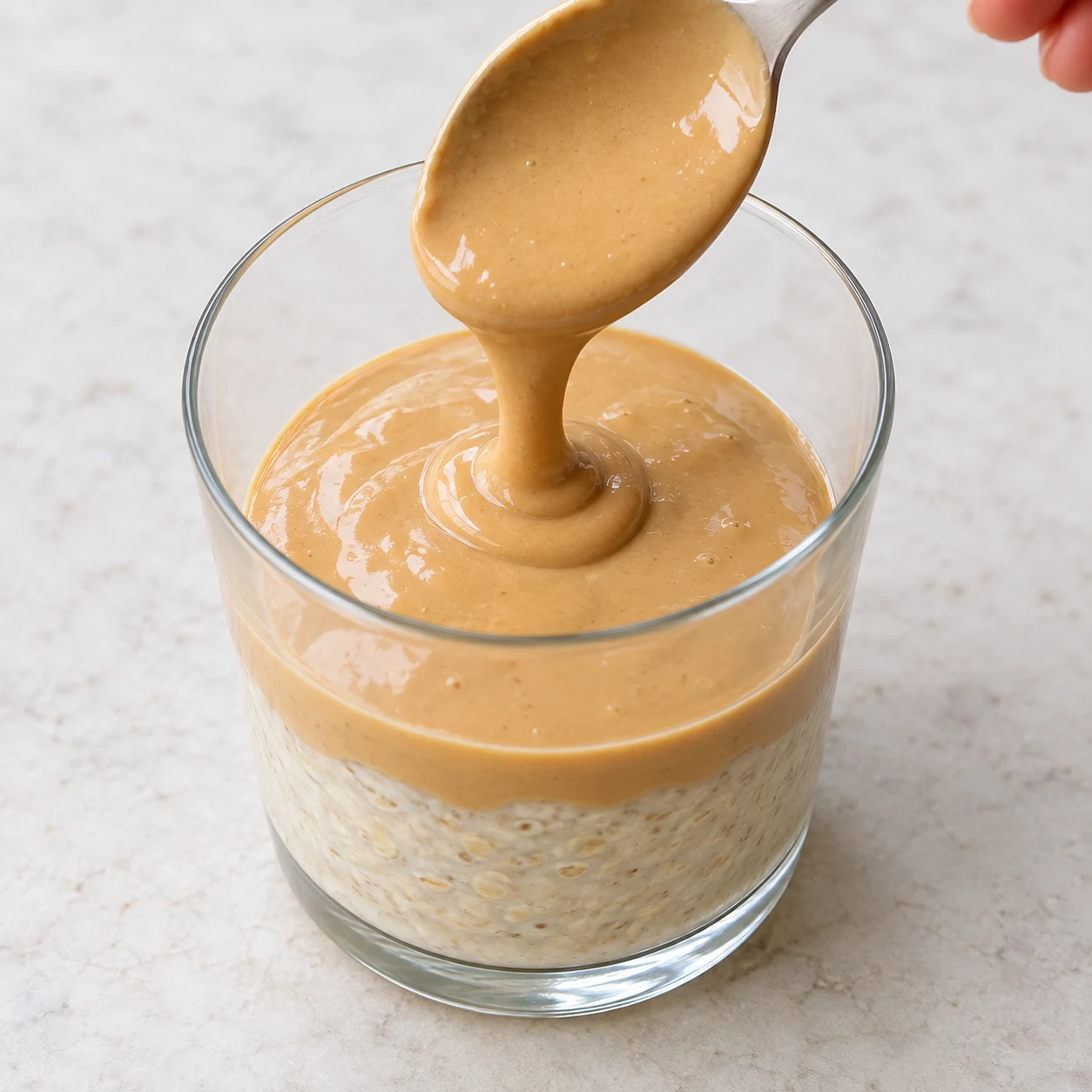 Photographie de cette seule phase : Verser la moitié de la ganache sur le porridge. Garder le reste pour la deuxième série de couches. État final : Une couche beige de ganache recouvre la première couche de porridge. Recette bis : base à l’avoine crémeuse, sans graines de chia ni poudre protéinée. Référence originale pour le montage, adaptation documentée pour les ingrédients.