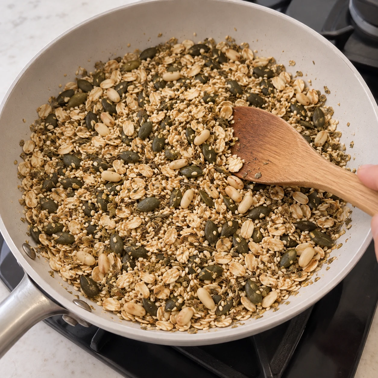 Dans une poêle chaude, fais revenir à sec 100 g de flocons d’avoine, 20 g de sésame, 30 g de graines de courge, 30 g de graines de courge supplémentaires, 30 g de pignons, et 1 c. à café de chacun : origan, herbes de Provence et thym. Poursuis jusqu’au crépitement. Ne montrer que le granola, aucune tomate ni base blanche. Geste décrit par la recette d’origine, non filmé.