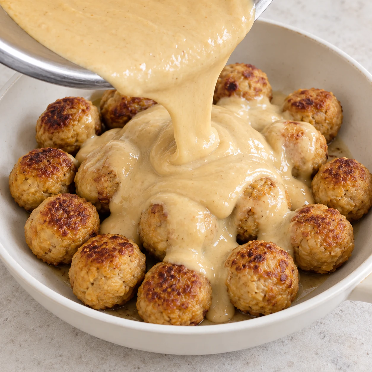 Sauce beige crémeuse versée sur les boulettes dorées.