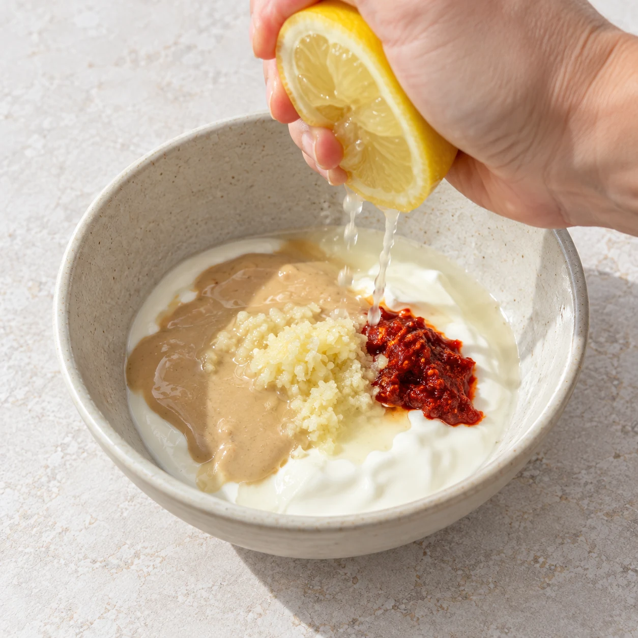 Main adulte anonyme pressant un demi-citron au-dessus du petit bol de sauce encore non mélangée.