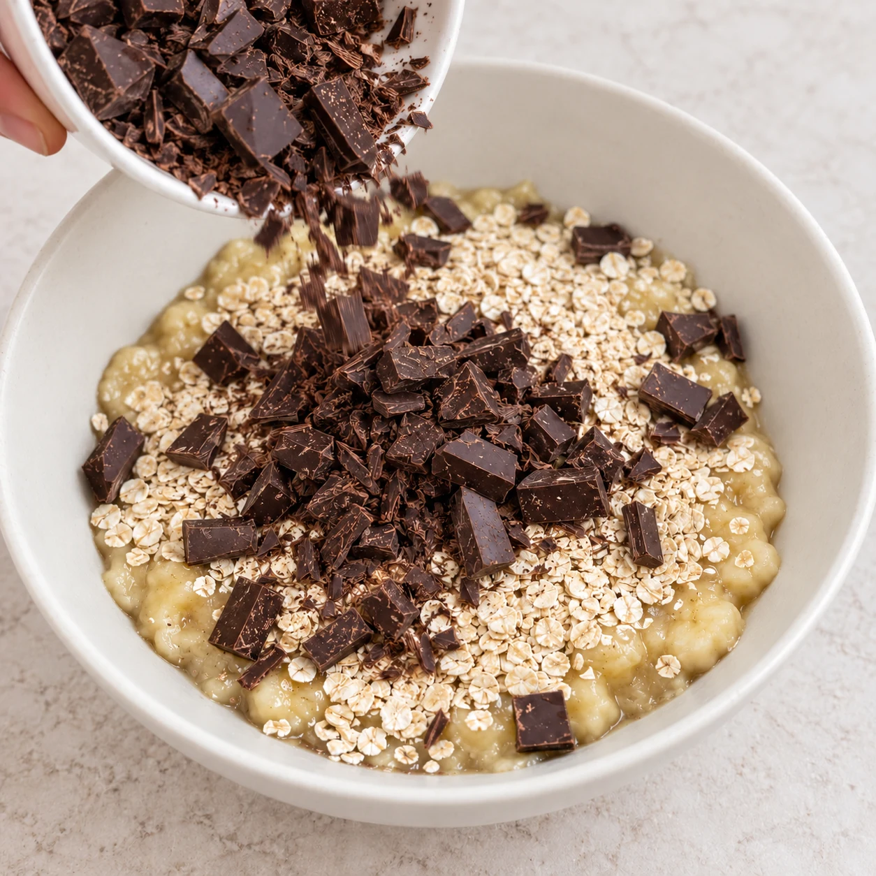 Verse les morceaux de chocolat noir sur les flocons et la banane. État attendu : Le chocolat haché est ajouté au saladier avec les deux autres ingrédients.