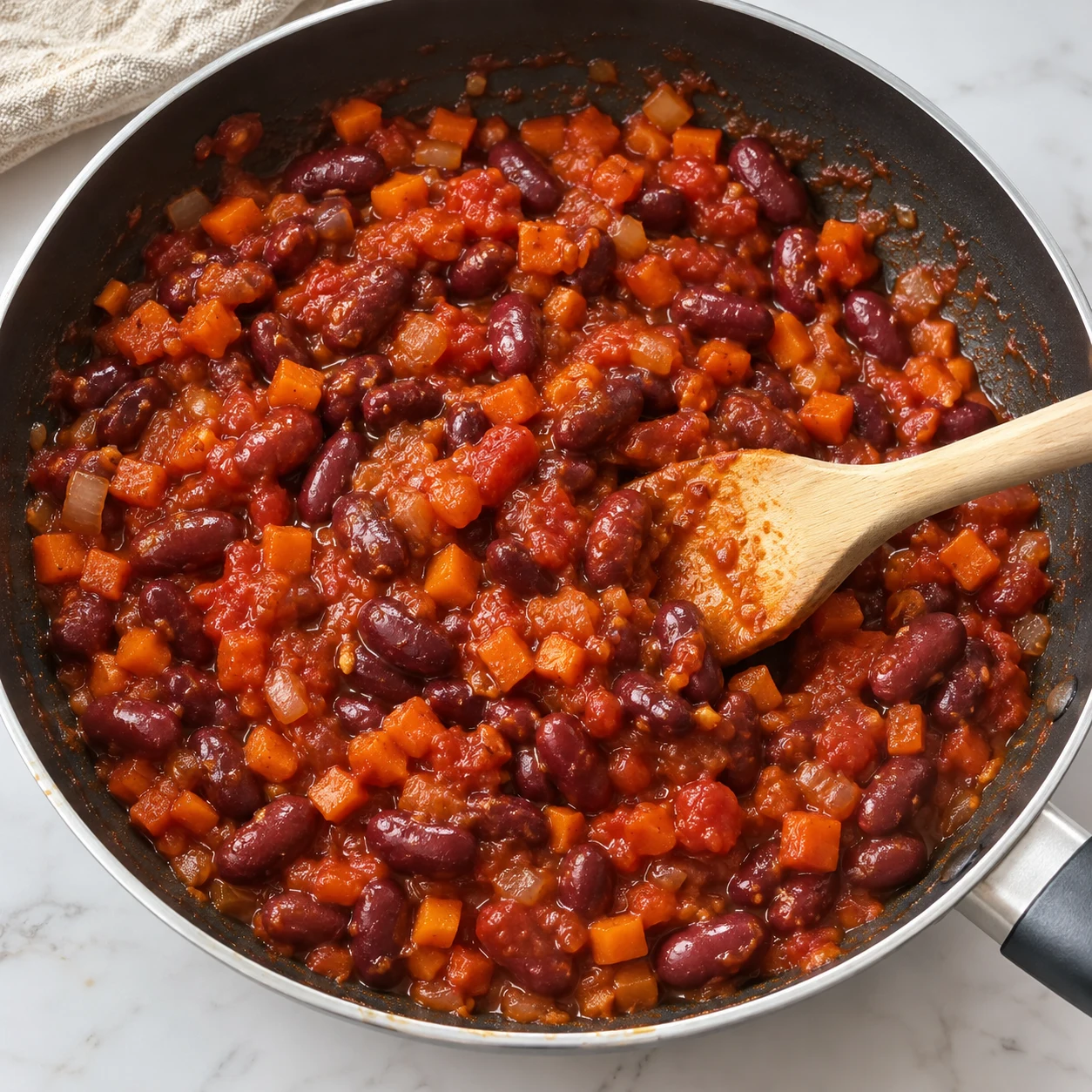 Spatule mélangeant haricots rouges entiers dans sauce tomate épaisse et petits dés orange.