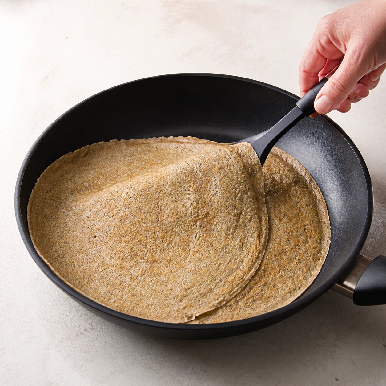 Galette de blé noir terminée, souple et brun-gris, pliée sur une assiette en grès clair.