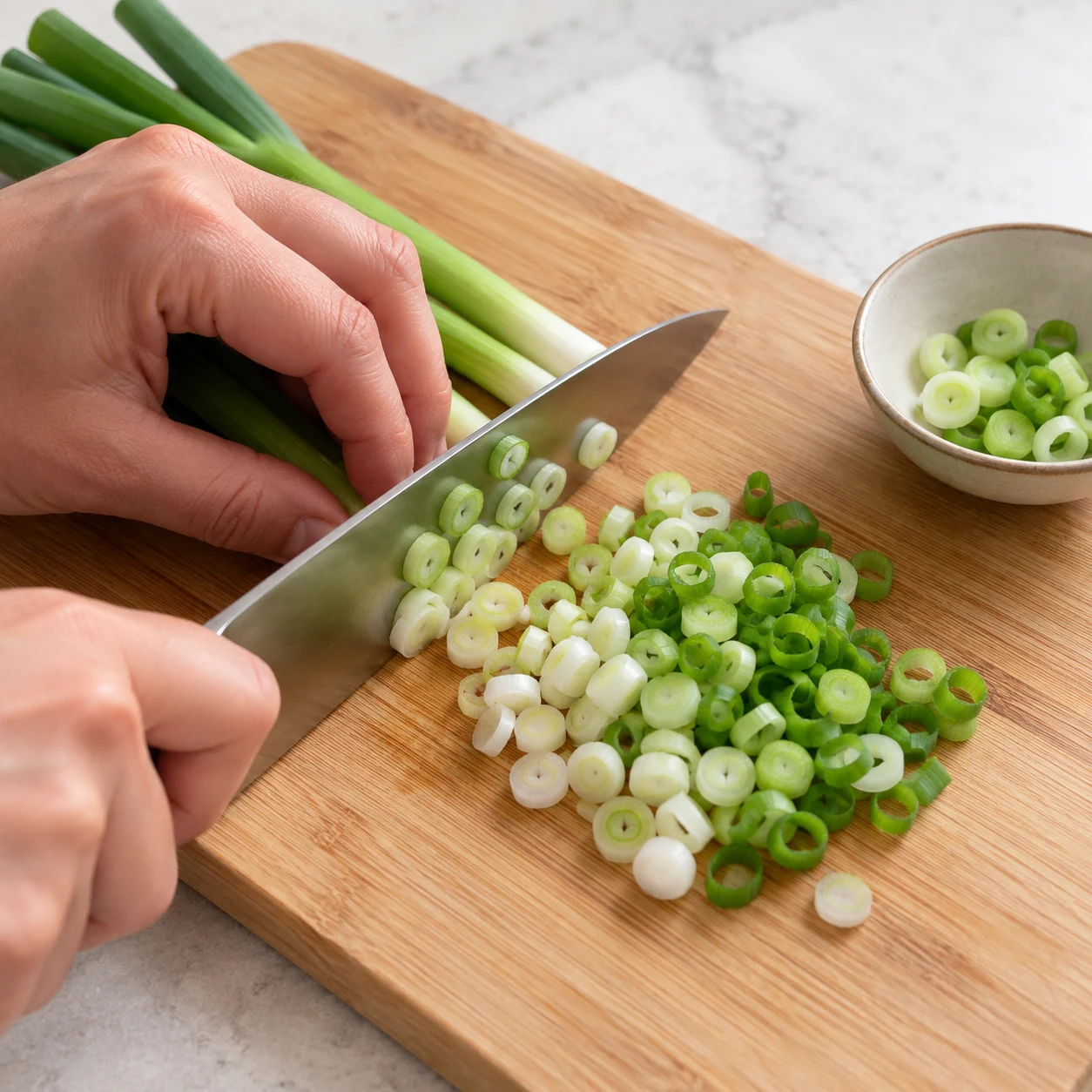 Émincer les oignons nouveaux. Émince finement les 2 oignons nouveaux sur une planche stable. Garde quelques rondelles pour la finition. Une seule action ; uniquement les ingrédients déjà présents à cette étape. Photographie carrée de livre de cuisine, sans personne identifiable ni texte.
