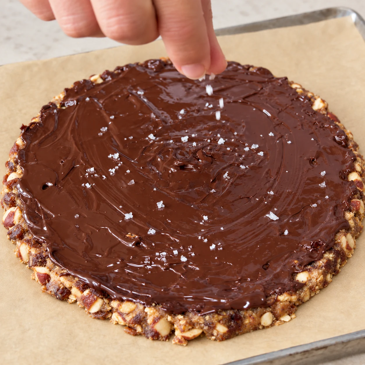 Main anonyme saupoudrant quelques cristaux de sel sur chocolat encore souple.