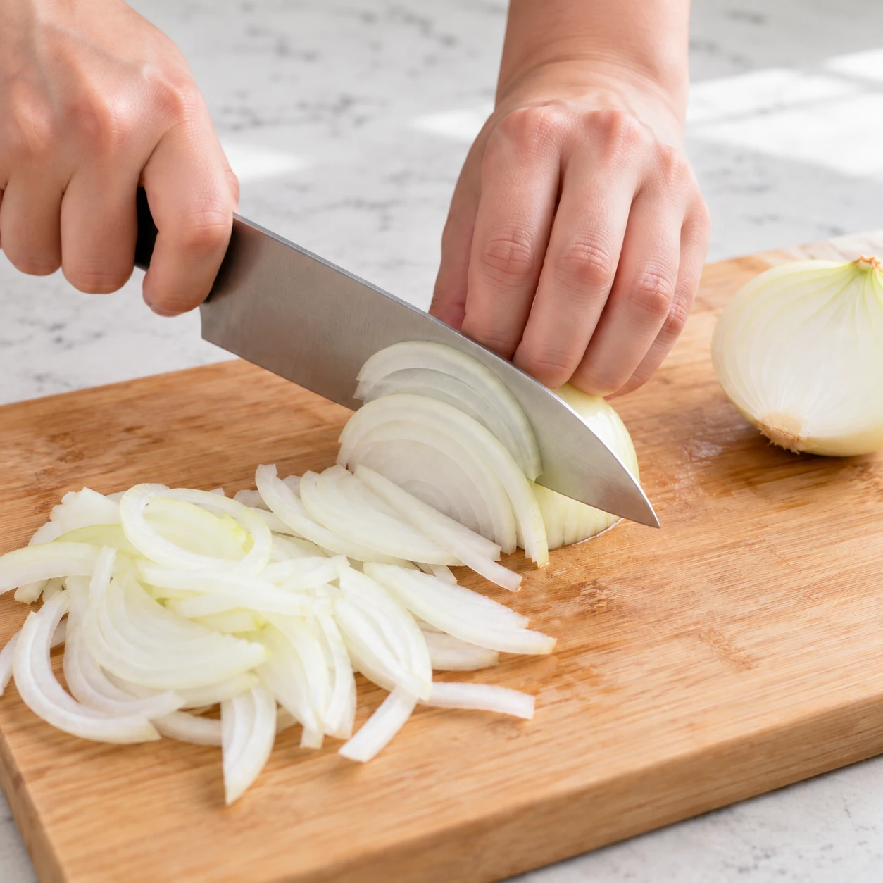 Émince l’oignon en fines lamelles sur une planche stable, avec les doigts repliés derrière la lame. État visible : L’oignon est émincé en fines lamelles.